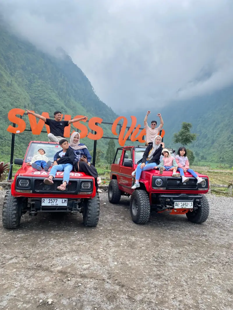 Dua keluarga dengan anak-anak duduk di atas dua jeep wisata merah di spot foto Swiss View