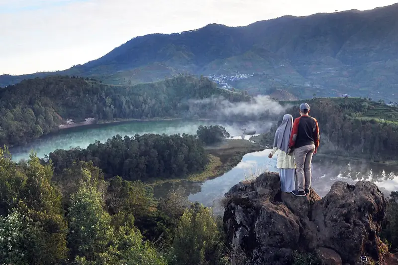 Dua orang berdiri di batu memandang Telaga Warna dan Telaga Pengilon yang berkabut